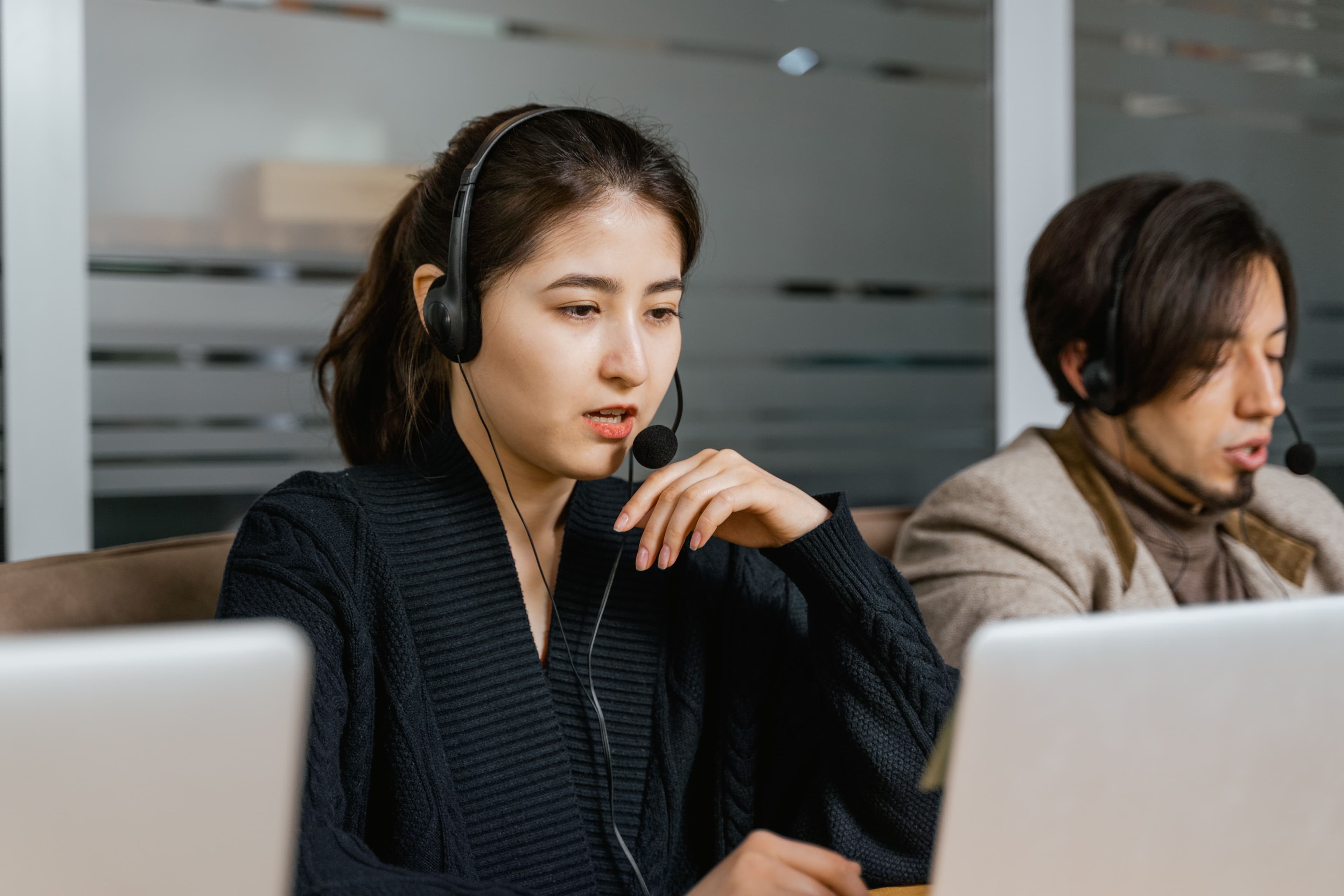 Two support professionals wearing headsets while working at their laptops